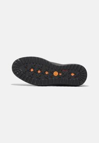 Soletta di scarpa nera in gomma con un motivo a tasselli testurizzato, caratterizzata da accenti arancioni e un logo circolare al centro, progettata per aderenza e durabilità.