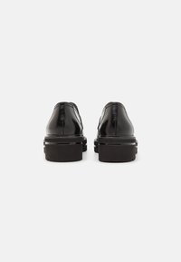 Scarpe in pelle nera con rifinitura liscia, punta arrotondata e suola spessa con un leggero rialzo sul tallone. Design semplice, senza motivi visibili.