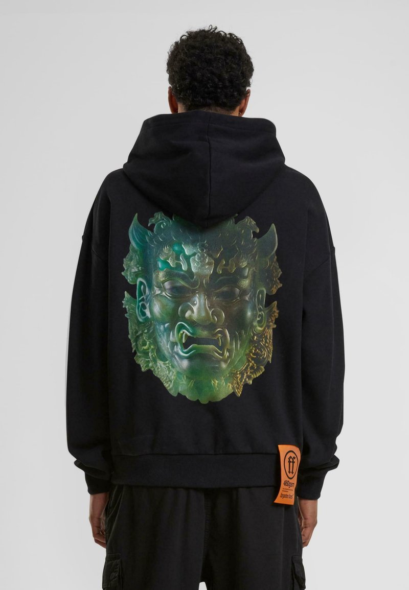 Sweat à capuche noir avec un grand graphique coloré d'un visage au dos, avec une surface texturée et une étiquette orange en bas.