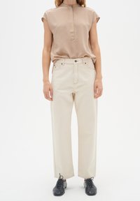 Beige, kortärmad blus med krage, som matchas med högmidjade, raka, off-white byxor. Svarta snörskor fulländar outfiten.