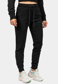 Zwarte sweatpants met een koordje in de taille, ribbelmanchetten, zijzakken en geborduurde details. Gepaarde met witte en mintkleurige sneakers.