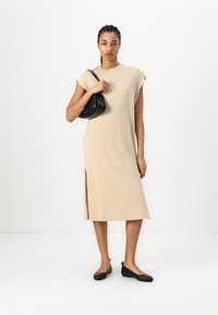 Robe beige, longueur genou, avec des manches courtes et une fente sur le côté. Associée à un sac à main noir et des ballerines noires. Tissu lisse et léger.