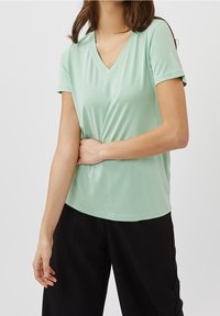 Mintgrøn V-hals T-shirt lavet af blødt, letvægtsstof. Korte ærmer, afslappet pasform og glat tekstur. Kombineret med sorte bukser.