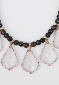 Collana con perle rotonde nere, accenti dorati e pendenti a forma di foglia rosa con texture sfaccettata ed elegante silhouette.