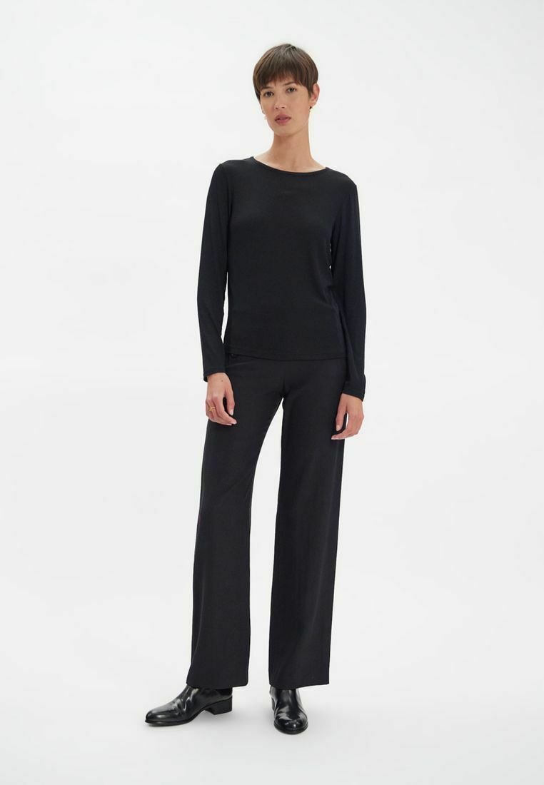 Haut à manches longues noir et pantalon large en tissu léger et lisse. La tenue est complétée par des bottines noires.