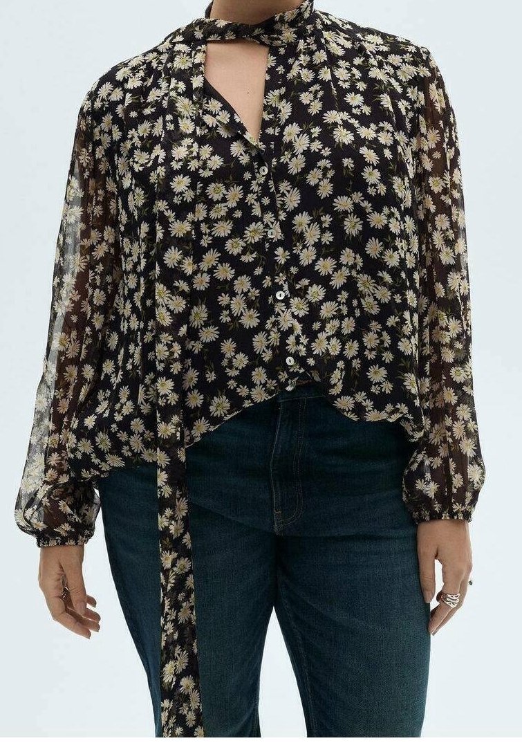 Blouse noire transparente avec imprimé marguerites, manches longues, fermeture à nouer au col et ourlet arrondi. Design à boutons.
