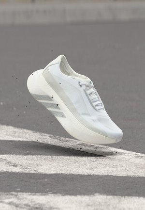 Weißer Sportschuh mit dicker Sohle, der über einer Asphaltstraße mit weißen gestrichenen Linien und kleinen Ablagerungen darunter schwebt.