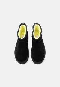 Botines negros de ante con forro interior amarillo y suela de goma. Superficie lisa sin herrajes ni acentos visibles.