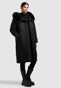 Melna pūkaina jaka ar mākslīgās ādas apkakli, ar garām piedurknēm, ar rāvējslēdzēju priekšā un sānu kabatām. Valkāta ar melnajām leginngiem un kurpēm ar šņorēm.