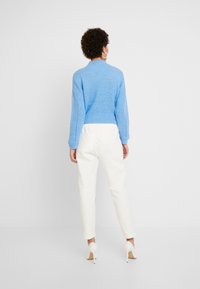 Maglione lavorato a maglia azzurro chiaro con colletto alto e maniche lunghe, abbinato a pantaloni bianchi a sigaretta e scarpe con tacco alto bianche.