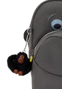 Zaino grigio realizzato in tessuto strutturato, con una grande decorazione a forma di occhio e un portachiavi a forma di gorilla nero peloso con una faccia marrone e piccoli dettagli.