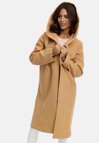 Beige gewatteerde jas met capuchon, gemaakt van zacht materiaal, met een relaxte pasvorm, grote voorzakken en een minimalistisch ontwerp.