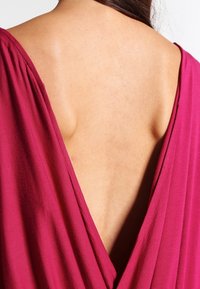 Mauve V-Ausschnitt-Teil mit drapiertem Stoff, der über einen tiefen Rückenschnitt und eine weiche Textur verfügt, die Haut- und Schulterkonturen zeigt.