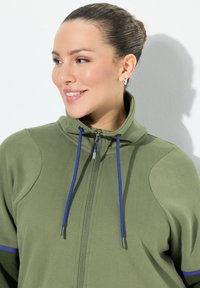Olive green hooded jacket with a full zipper, contrasting blue drawstrings, and a smooth texture. Features a high collar and side panels.