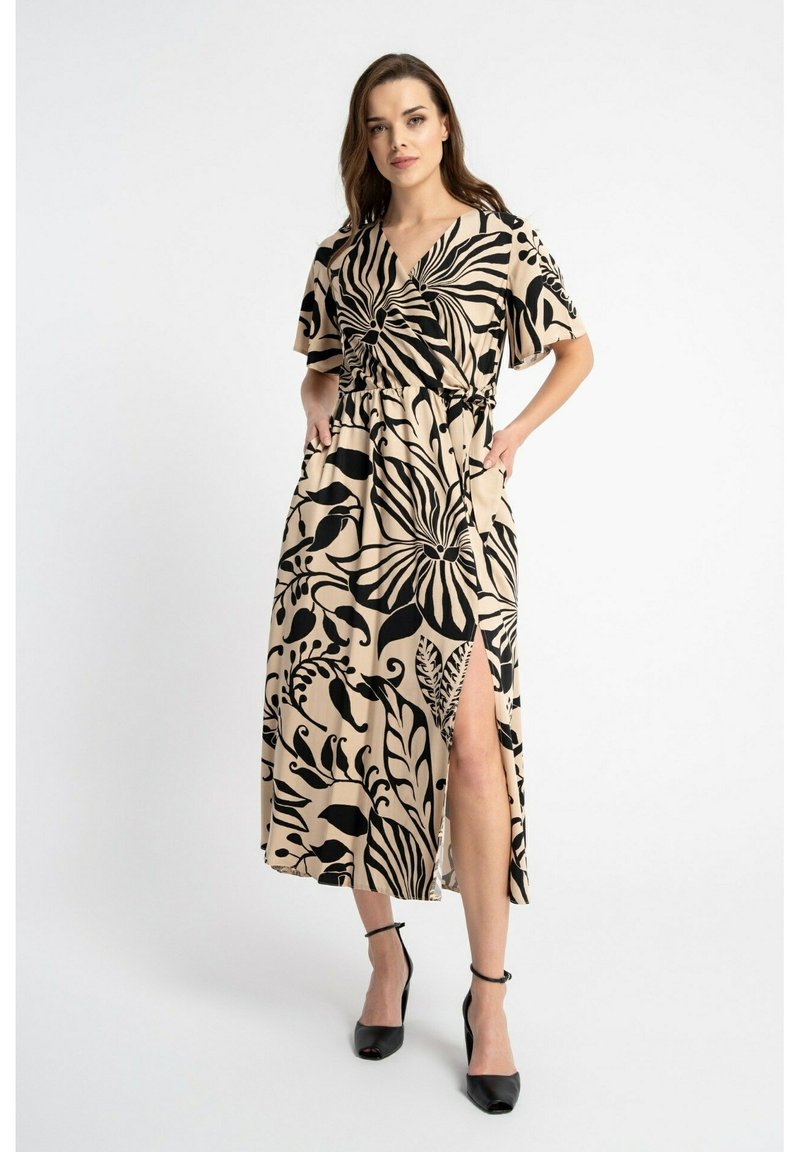 Beżowa sukienka w kwiatowy wzór z krótkimi rękawami, luźnym krojem i bocznym rozcięciem. W zestawie z czarnymi butami na obcasie. Gładka tekstura materiału.