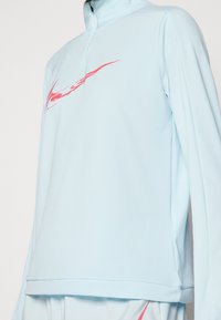 Jasnoniebieski długi rękaw sweter z wysokim kołnierzem, z różowym logo Nike z przodu i gładkiego, elastycznego materiału.