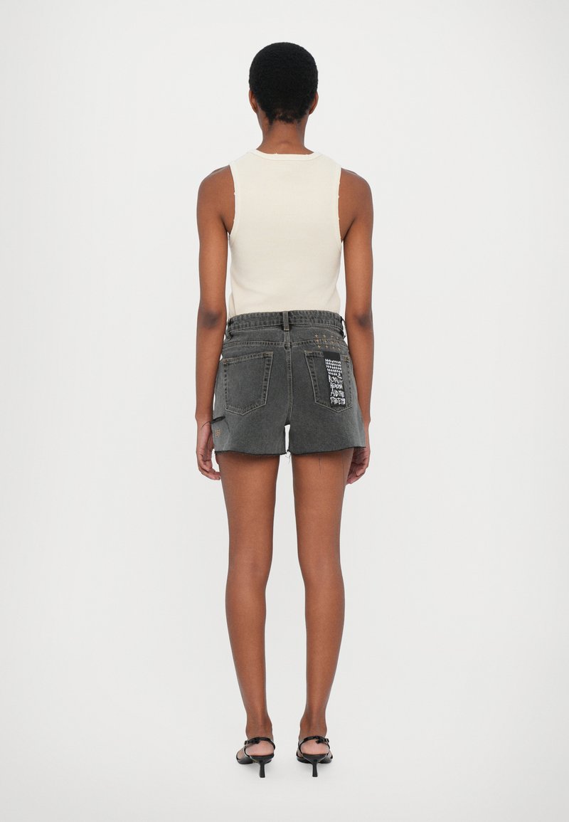 Shorts di denim nero con orlo sfrangiato e due tasche posteriori, caratterizzati da dettagli testuali stampati sulla tasca destra e una vita piatta.