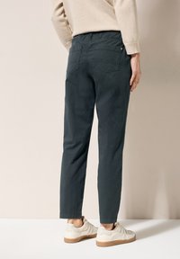 Dark green, tapered trousers with a casual design and elastic waistband. Back features two pockets; paired with light sneakers.