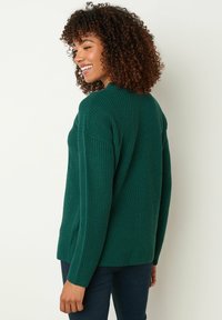 Grüner Strickpullover mit strukturiertem Muster, langen Ärmeln und seitlichen Schlitzen. Verfügt über eine lockere Passform und gerippte Details an den Bündchen und am Halsauschnitt.