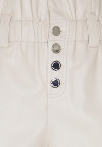 Pantalon en fausse cuir couleur crème, doté d'une texture lisse, d'une ceinture élastique et de trois boutons métalliques avec des marqueurs distincts.