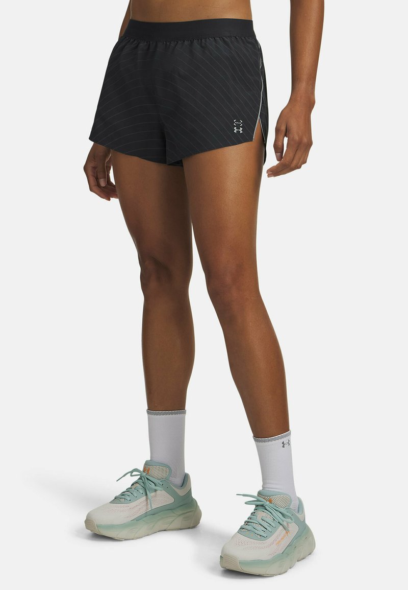 Pantaloncini atletici neri con righe bianche sottili, dotati di spacco laterale e una morbida fascia elastica in vita, abbinati a scarpe da corsa di colore chiaro.