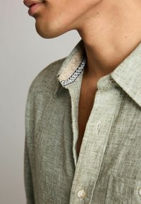 Jasnozielona koszula w kratę z zapinanym kołnierzykiem, z teksturowanym wewnętrznym kołnierzem ozdobionym granatowo-kremowym zygzakowatym wzorem.