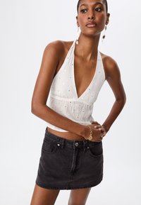 Witte haltertop met open rug, voorzien van geborduurde details en zilveren accenten, gecombineerd met een high-waisted zwarte denim minirok.