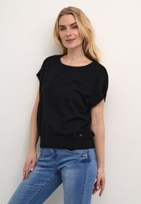 Černý krátký rukávový top s kulatým výstřihem a žebrovaným lemem. Doplněno o světle modré džíny s odřenými detaily a tvarovaným střihem.