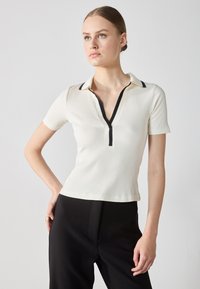 White ribbed short-sleeve polo shirt with a black zipper and collar accents, featuring a fitted design and a deep V-neckline.