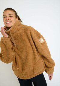 Pullover in pile marrone con colletto alto, maniche lunghe e superficie testurizzata. Presenta tasche frontali e una patch con il logo sulla manica.