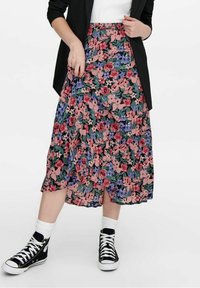 Gonna midi floreale con sfondo scuro, caratterizzata da motivi rosa, viola e verdi; abbinata a sneakers nere e calzini bianchi alla caviglia.