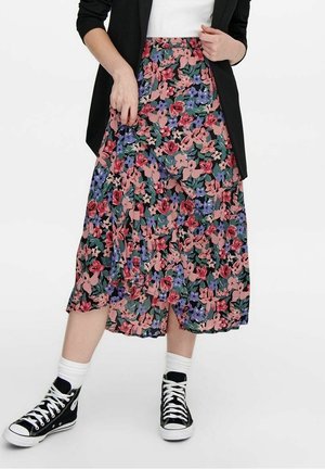 Jupe midi florale avec un fond sombre, ornée de motifs roses, violets et verts ; portée avec des baskets noires et des chaussettes blanches.
