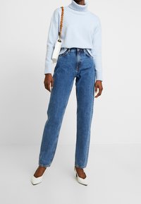 Ljusblå polotröja, kombinerad med högmidjade blå jeans. Vita spetsiga klackar och en liten vit väska med kedjerem.