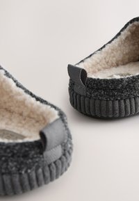 Sive tkanine copate z mehko, puhasto notranjostjo. Imajo teksturirano zunanjost in črtast, rebrast podplat. Vključujejo tkaninske zanke kot detajle.