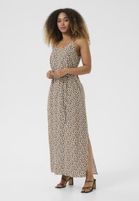 Maxi dress in light beige with a black leopard print, featuring thin straps, a v-neck, and a side slit. Paired with black block-heeled sandals.