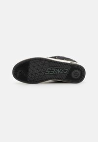 Black sneaker sole with textured rubber, featuring a patterned grip and a prominent logo. Subtle off-white accent along the edge.