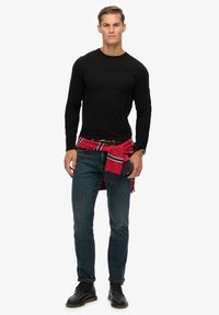Zwarte longsleeve shirt, blauwe denim jeans, rode trui om de taille geknoopt, en zwarte leren laarzen. Eenvoudig ontwerp, casual look.