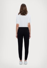 Svarta joggers med en smal passform, elastisk midja och muddar, i kombination med en enkel vit t-shirt med kort ärm och vita sneakers.
