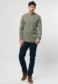 Olijfgroene langemouwenshirt met een textuurpatroon. Gecombineerd met donkerblauwe jeans en een paar bruine veterschoenen. Eenvoudig ontwerp en aansluitende pasvorm.