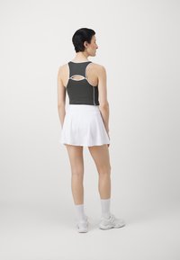 Sötétzöld sportosan szabott ujjatlan felső, fehér részletekkel, kivágott hátrésszel, fehér, bővülő szoknyával párosítva. A modellen fehér lábbeli van.
