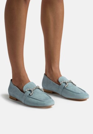 Mocassins en suède bleu clair avec une texture lisse, rehaussés d'une chaîne décorative en rhinestones sur le devant et d'une semelle en bois plate.
