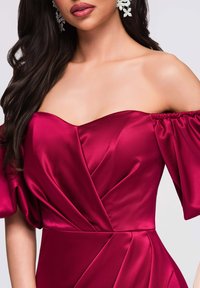 Robe en satin bordeaux décolletée avec manches bouffantes, dotée d'un détail torsadé à l'avant et d'une texture lisse. Des boucles d'oreilles florales scintillantes viennent accentuer le tout.