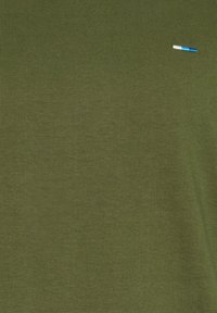 Tissu vert olive avec un petit détail brodé en fil bleu et blanc près du coin supérieur droit.