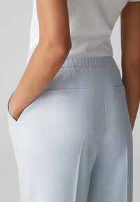 Pantalon bleu clair avec une texture lisse, une taille élastique et deux poches arrière, vu de côté, mettant en avant la forme et le design.