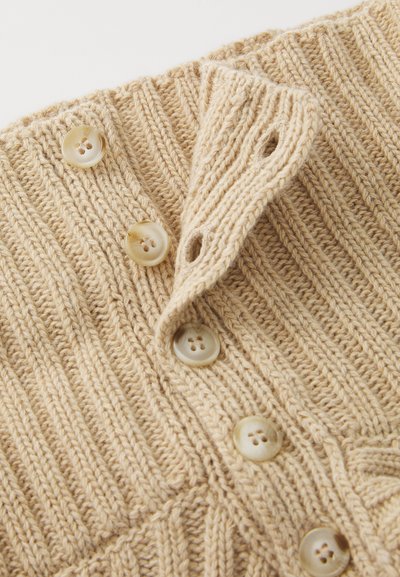 Cardigan bej tricotat, cu textură côtată, având cinci butoane rotunde de nuanță crem și un guler pliat cu găuri pentru butoane.