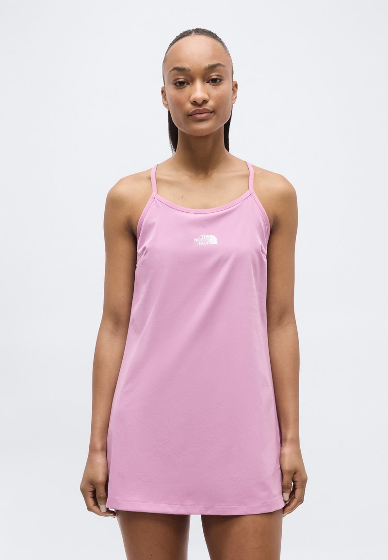 Γυναίκα που στέκεται μπροστά, φοράει ένα μωβ αμάνικο φόρεμα με λεπτούς ιμάντες και λευκό λογότυπο στο στήθος.