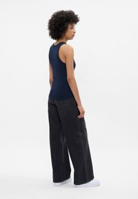 Marineblå tank topp med en tettsittende design, brukt sammen med løse, svarte vide bukser og hvite joggesko. Antrekket har en minimalistisk stil og subtile teksturer.