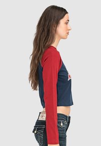 Gekürztes Langarmshirt mit einem navyfarbenen Körper und roten Ärmeln, einem runden Ausschnitt und einem dekorativen Logo auf der Vorderseite.