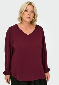 Burgundy long-sleeve top with a V-neck, made of smooth fabric. Features gathered cuffs and a loose, curved hem.