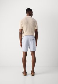 Beige knitted polo shirt, light blue textured shorts with pockets, and brown sandals, viewed from the back against a neutral background.
